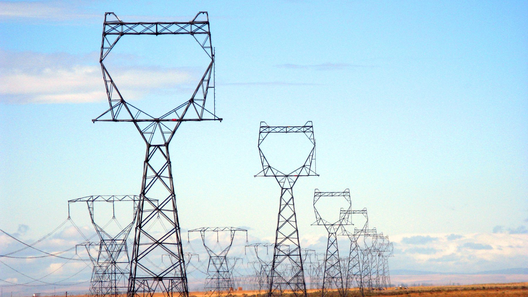 Rows of steel lattice transmission towers receding across dry sagebrush country under an open sky.